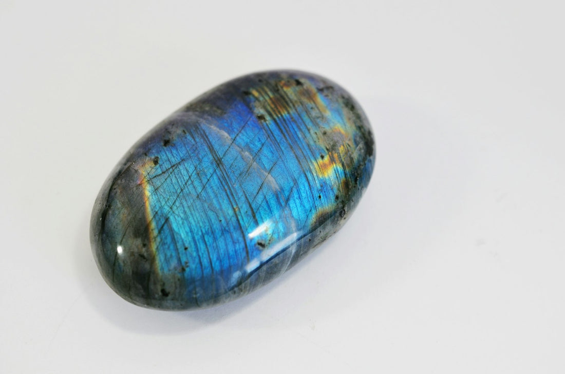 Polished labradorite stone showing blue and black iridescence on a white surface